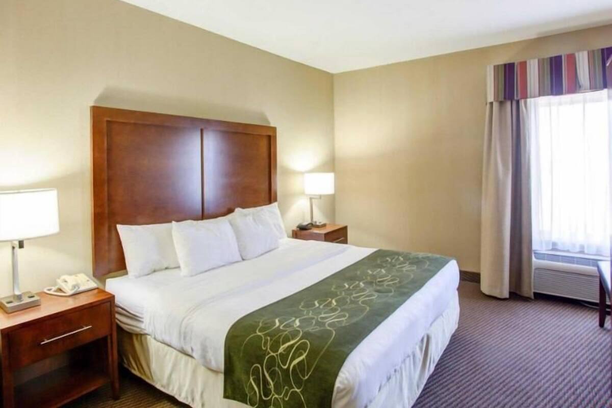 Ein Hotelzimmer mit einem großen Bett, zwei Nachttischen mit Lampen, einer grünen dekorativen Bettdecke und einem Fenster mit Vorhängen.