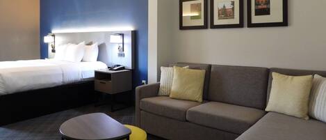 Una habitación de hotel con una cama, un sofá, una mesita y un reposapiés amarillo. Hay tres cuadros en la pared.