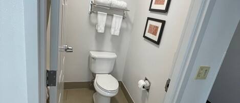 A small, clean bathroom with a toilet, a towel rack with towels, and two framed pictures on the wall.