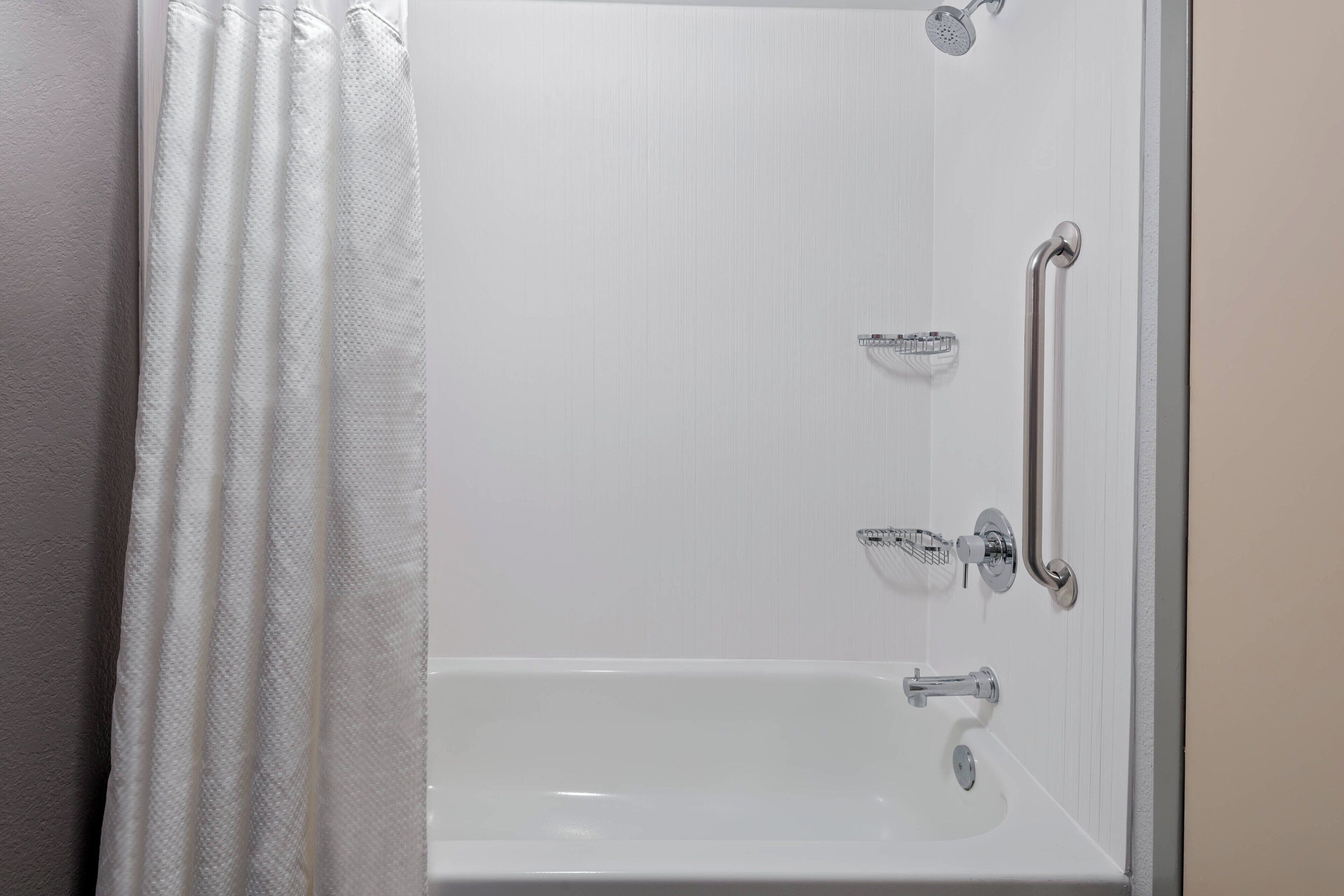 Une salle de bain blanche avec une baignoire, une douche et une barre d’appui.