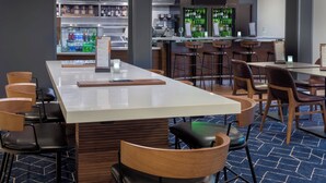 A modern bar area with a long counter, stools, and a refrigerated display case. - Courtyard by Marriott Tallahassee North/I-10 Capital Circle (Tallahassee)