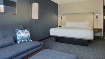 A modern hotel room with a large bed, a grey sofa, and a small table.