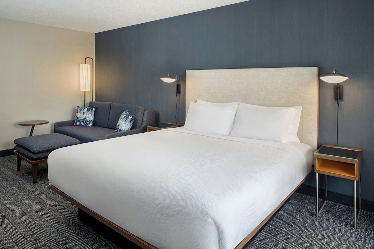 A hotel room with a large bed, a sofa, two bedside tables, and a lamp.