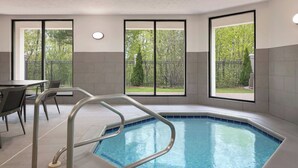 A swimming pool with metal railings, a dining area with chairs, and large windows with a view of greenery. - Courtyard by Marriott Traverse City (Traverse City)