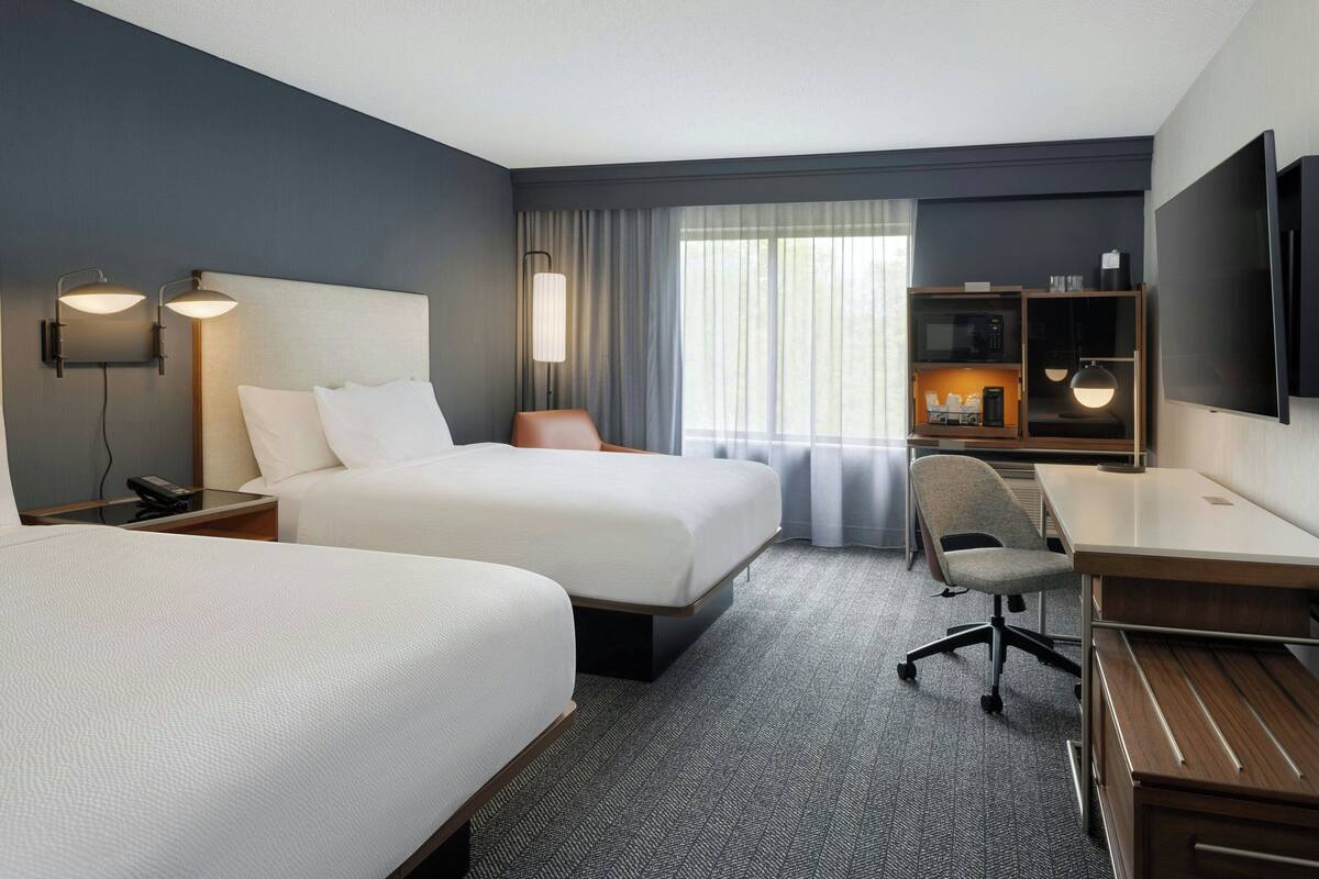 A hotel room with two beds, a desk, a chair, a TV, and a minibar.