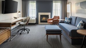 A modern hotel room with a flat-screen TV, a desk with a chair, a sofa with cushions, a fireplace, and a large window with curtains. - Courtyard by Marriott Traverse City (Traverse City)