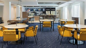 A modern dining area with round tables and yellow chairs, a bar area with stools, and a menu display. - Courtyard by Marriott Traverse City (Traverse City)