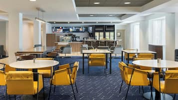 A modern dining area with round tables and yellow chairs, a bar area with stools, and a menu display.