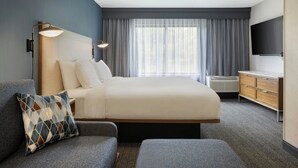 A hotel room with a large bed, a flat-screen TV, a desk, and a window with curtains. - Courtyard by Marriott Traverse City (Traverse City)