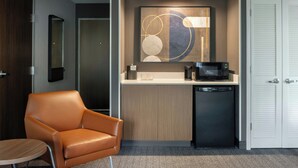 A compact hotel room with a kitchenette, a single chair, a small table, and a wardrobe. - Courtyard by Marriott Traverse City (Traverse City)