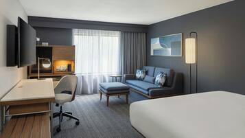 Een moderne hotelkamer met een bed, een bureau met stoel, een bank, een bijzettafeltje en een aan de muur bevestigde televisie.