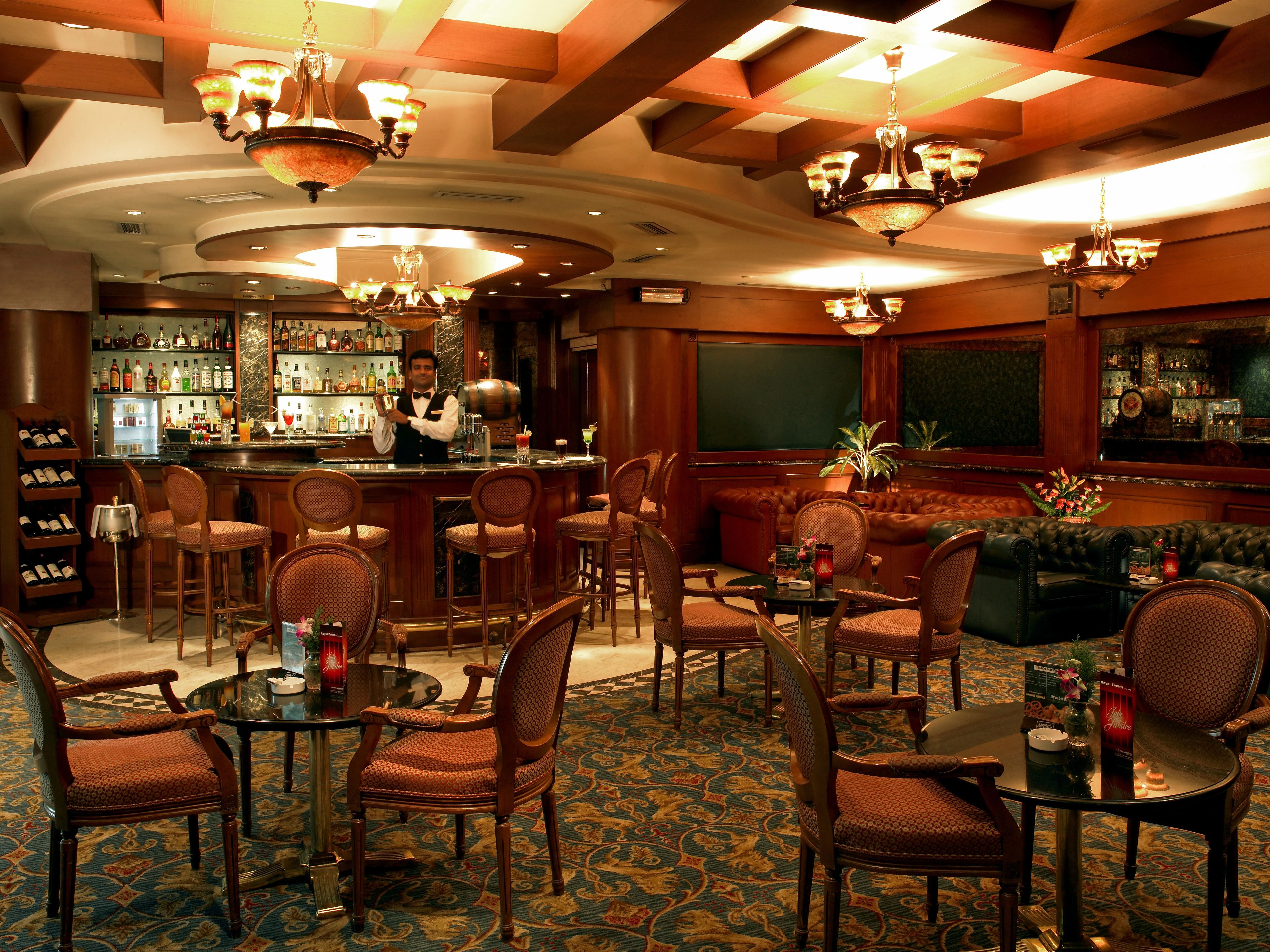 A bar area with a bartender, bar stools, and a variety of liquor bottles. There are also several chairs and a sofa in the seating area.