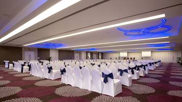A conference room with rows of white chairs with blue sashes, a patterned carpet, and modern ceiling lighting.