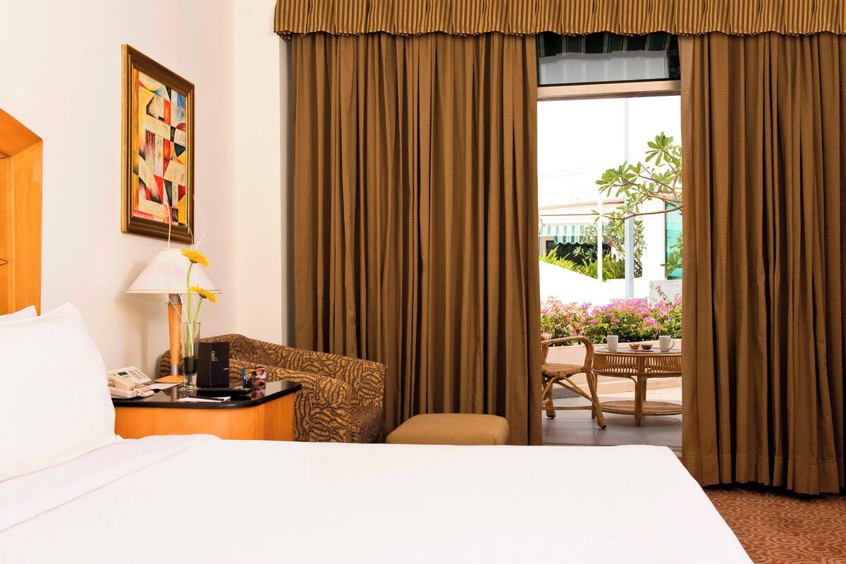 Habitación de hotel con cama, escritorio con lámpara, una silla y vista al exterior.