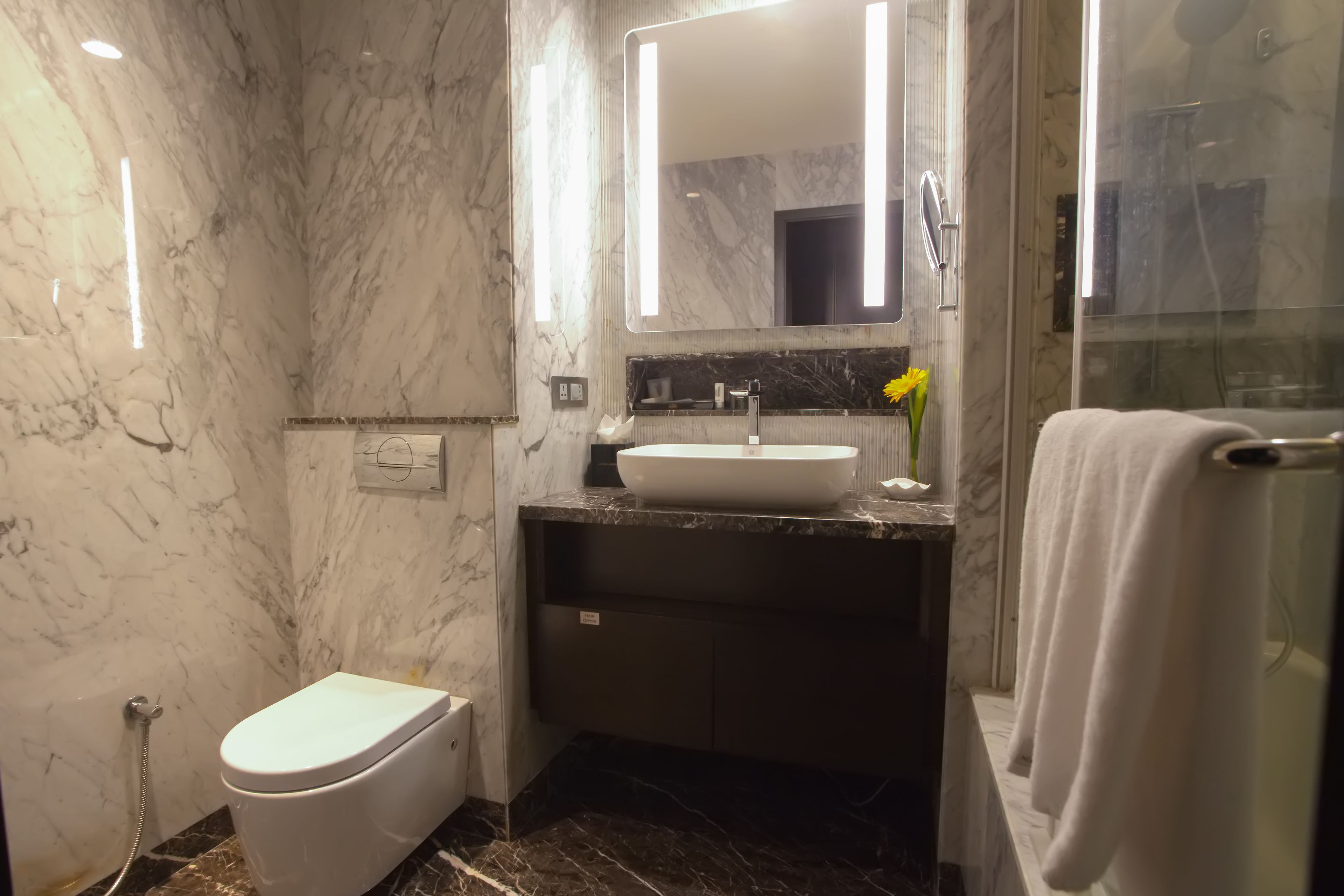 A bathroom with a marble wall, a white toilet, a sink with a marble countertop, and a glass shower enclosure.