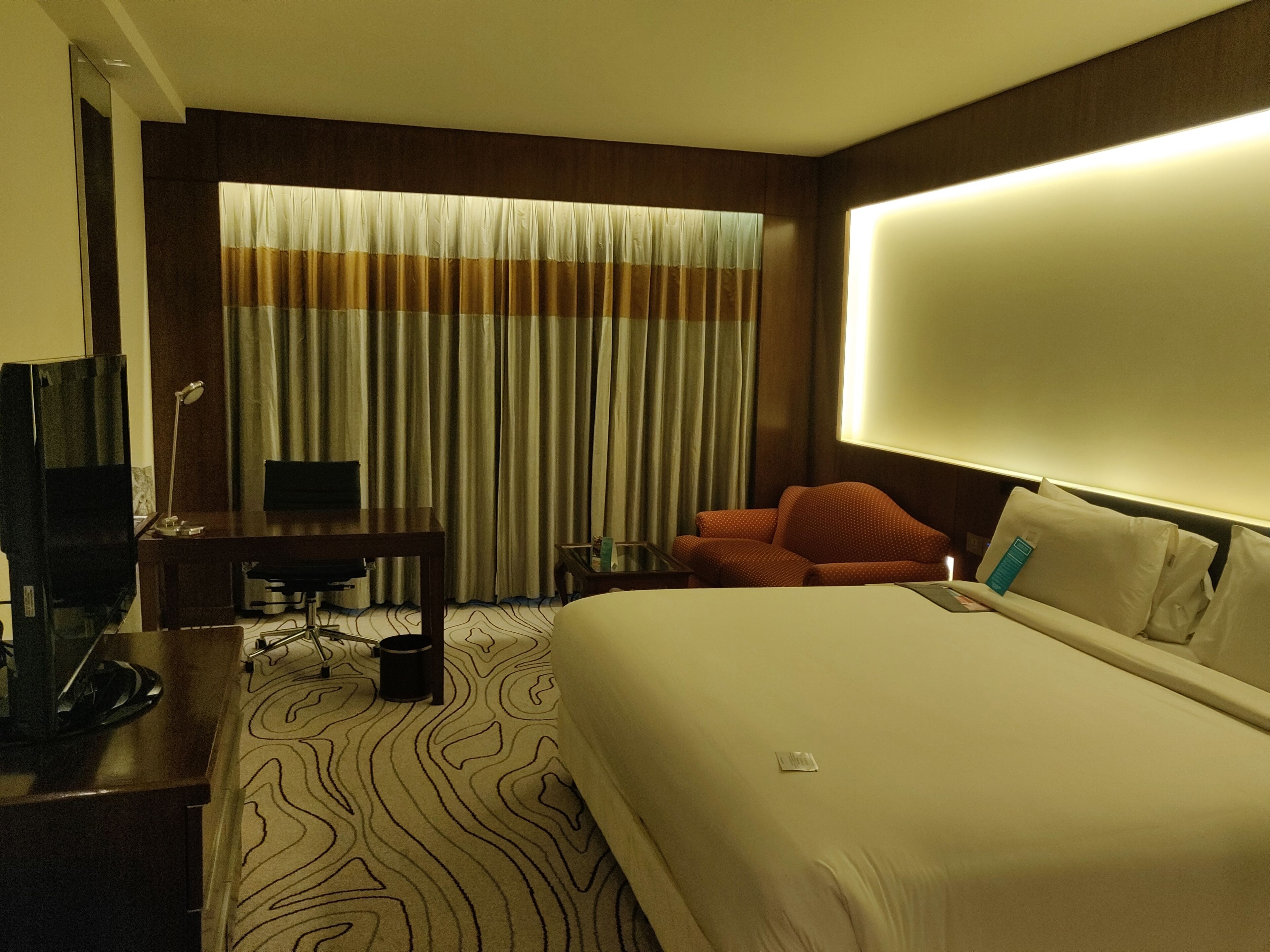 A hotel room with a large bed, a desk with a chair, a television, and a window with curtains.