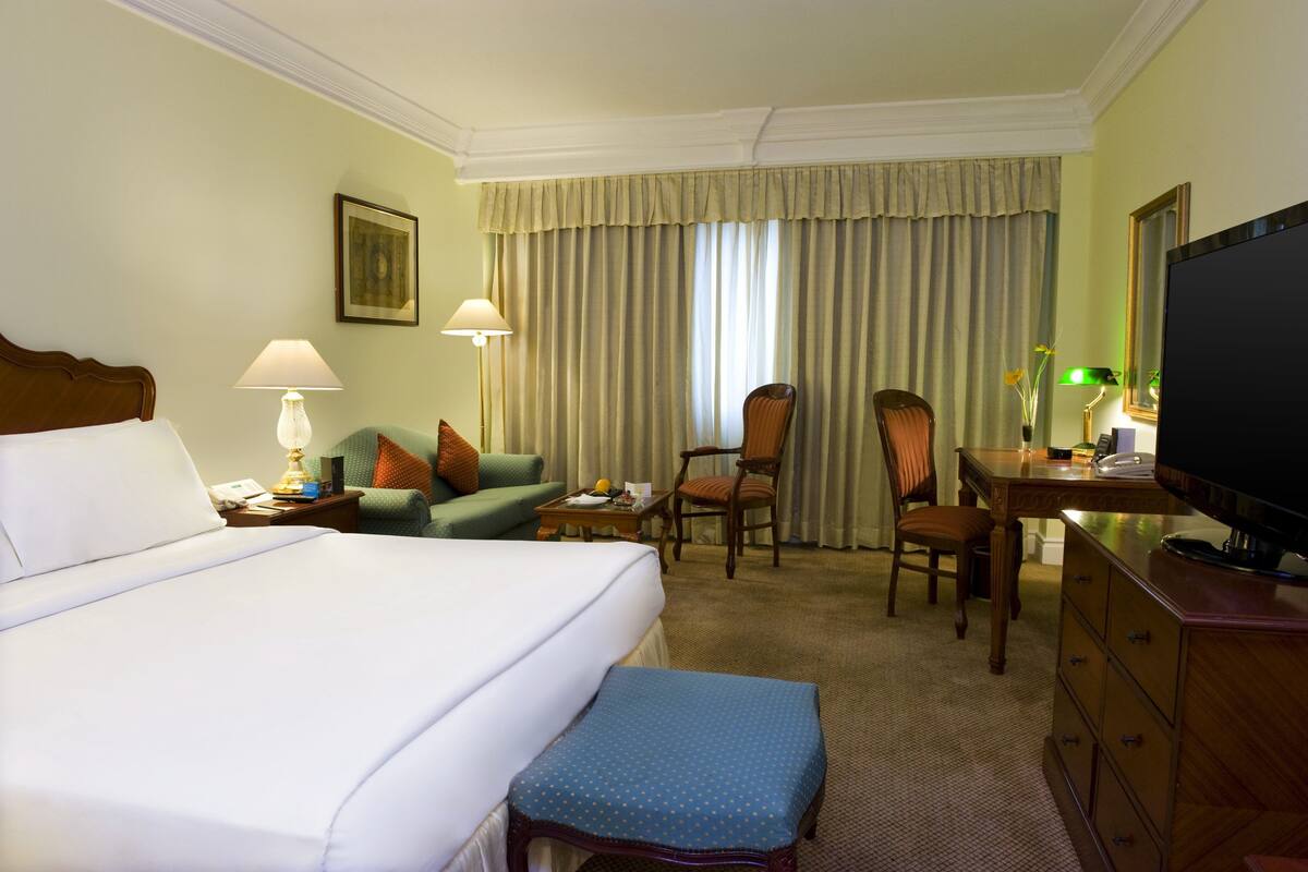 Habitación de hotel con una cama grande, un escritorio con televisor, una silla, una mesita y una lámpara.