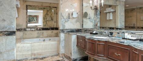 Un baño lujoso con piso de mármol, una bañera grande y un tocador con espejo.