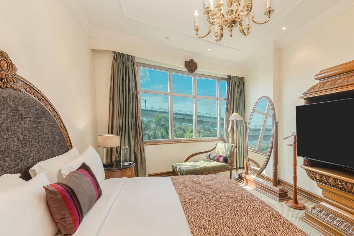 Habitación de hotel con una cama grande, televisión, candelabro, ventana con vistas y una silla.