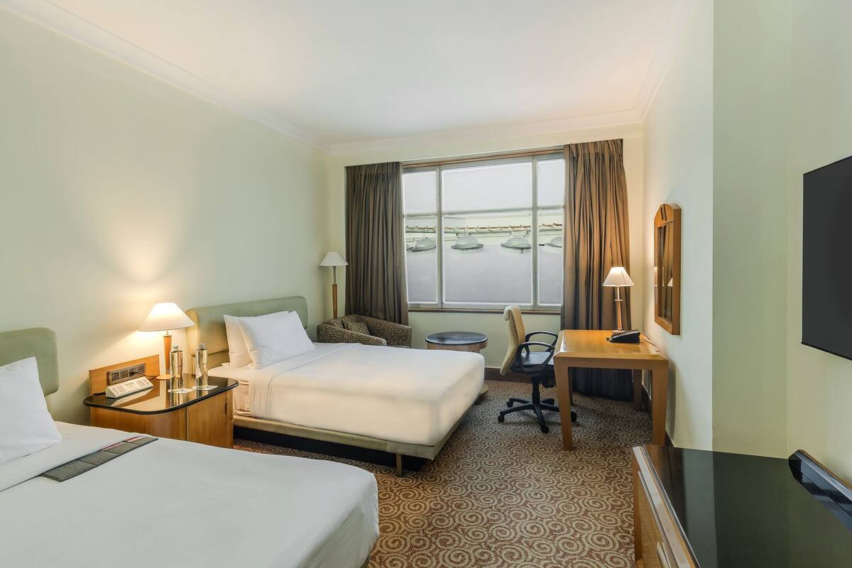 Habitación de hotel con dos camas, un escritorio, una silla, un televisor y una ventana con cortinas.