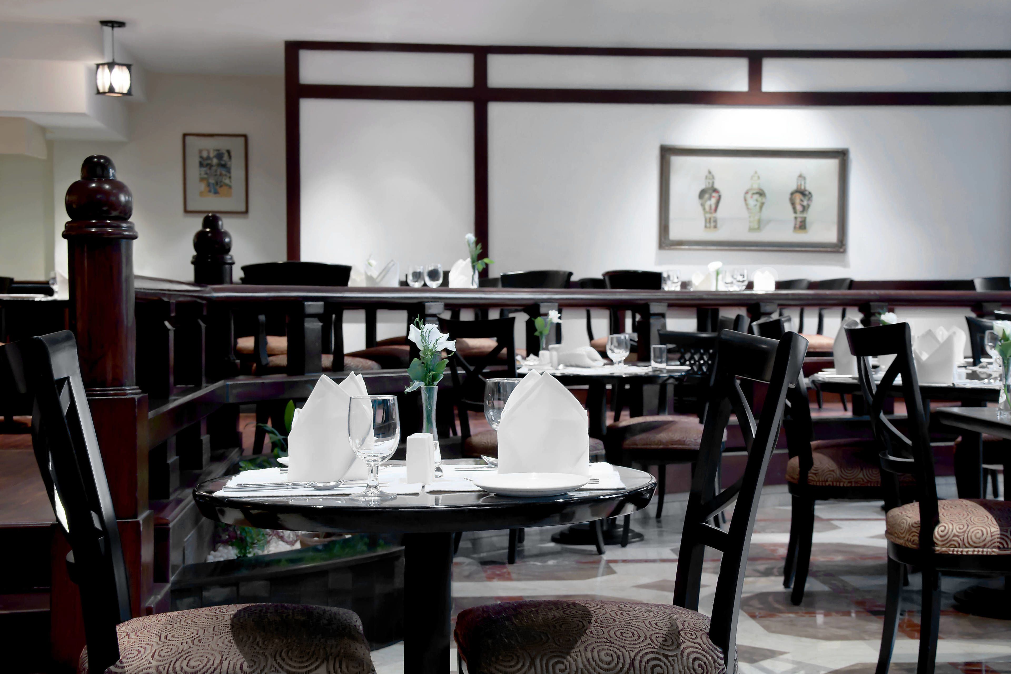 A restaurant with tables set for dining, chairs, and a decorative wall.