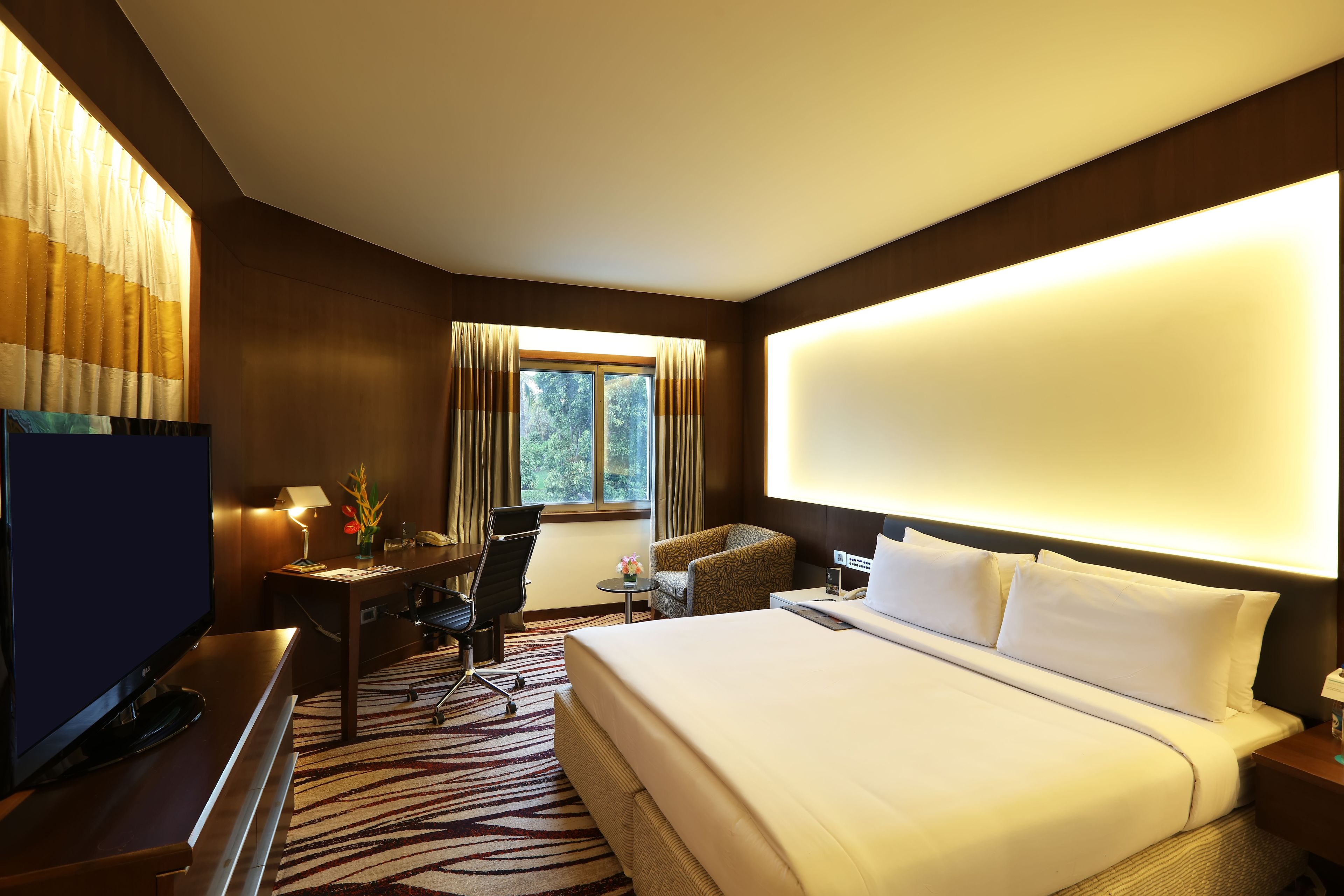 A hotel room with a large bed, a desk with a chair, a television, and a window with curtains.