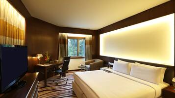 A hotel room with a large bed, a desk with a chair, a television, and a window with curtains.