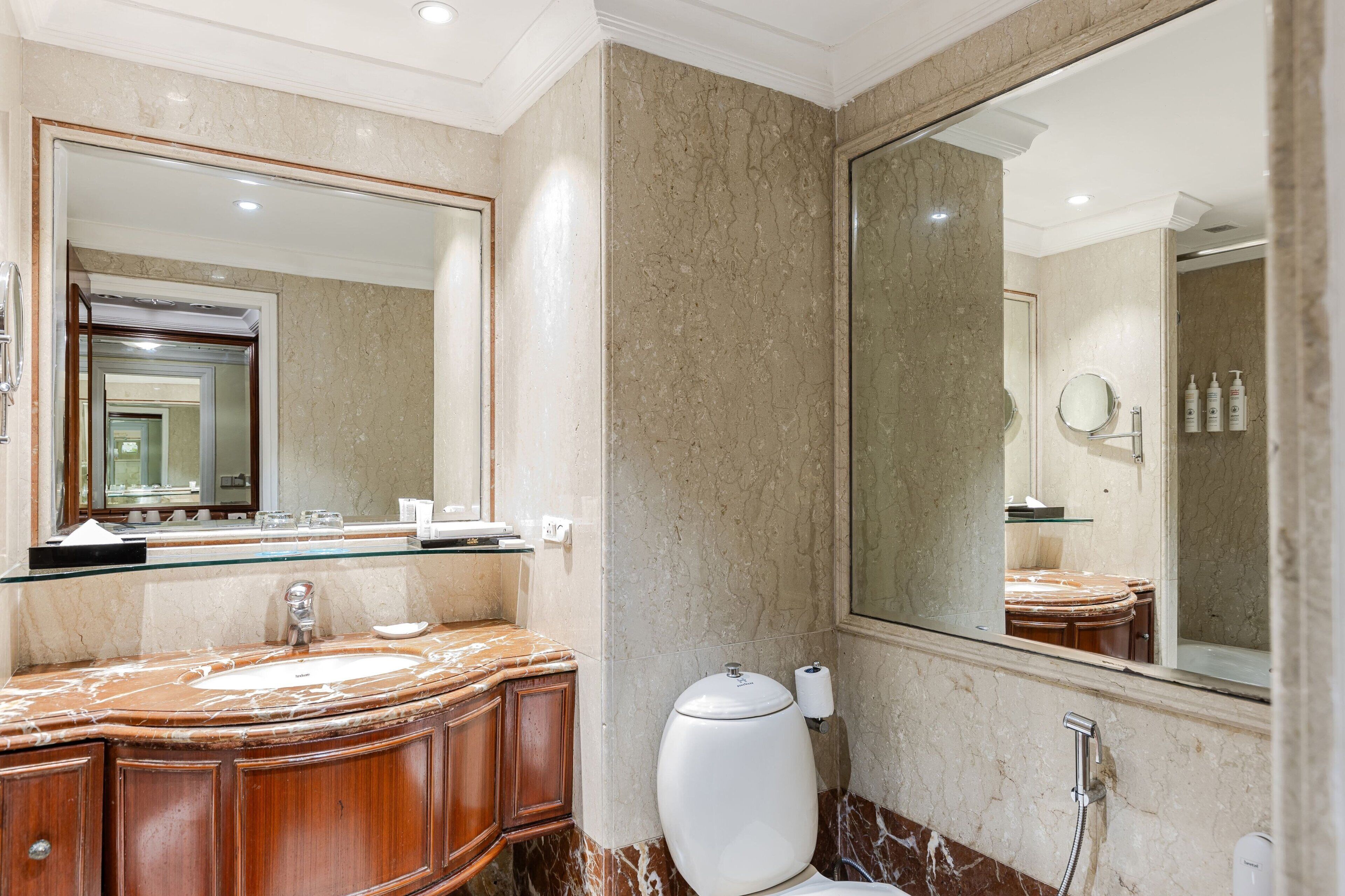 A bathroom with a marble sink, wooden vanity, a large mirror, and a toilet.