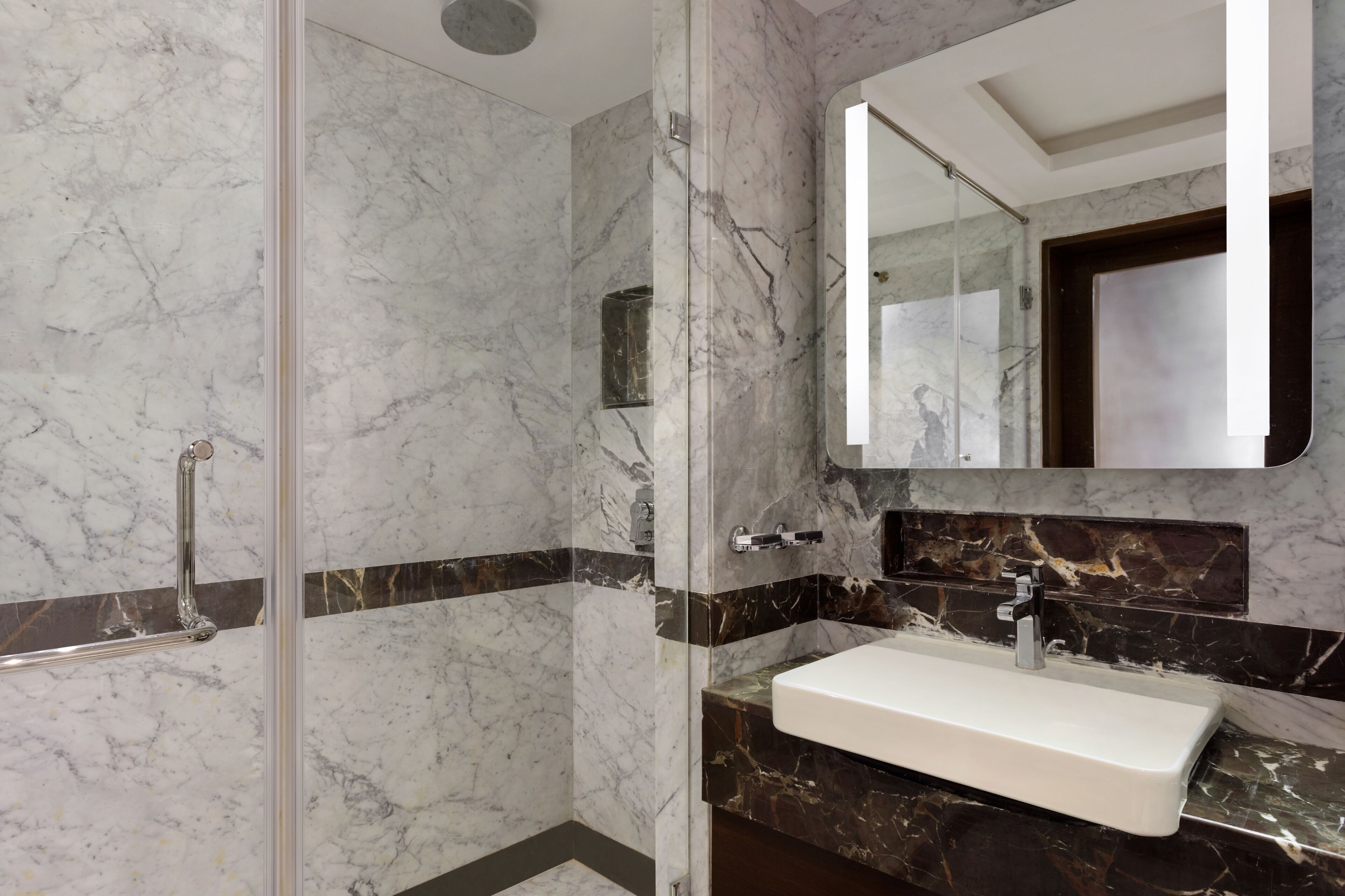 A bathroom with a glass-enclosed shower, a white sink, and a dark marble countertop.