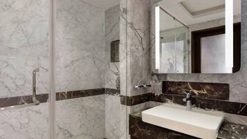 A bathroom with a glass-enclosed shower, a white sink, and a dark marble countertop.