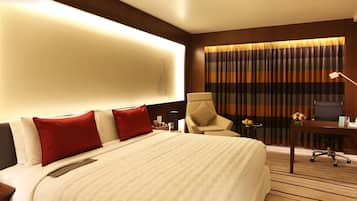 Une chambre d’hôtel avec un grand lit, un bureau avec une chaise, une lampe et une vue sur l’extérieur à travers les rideaux.