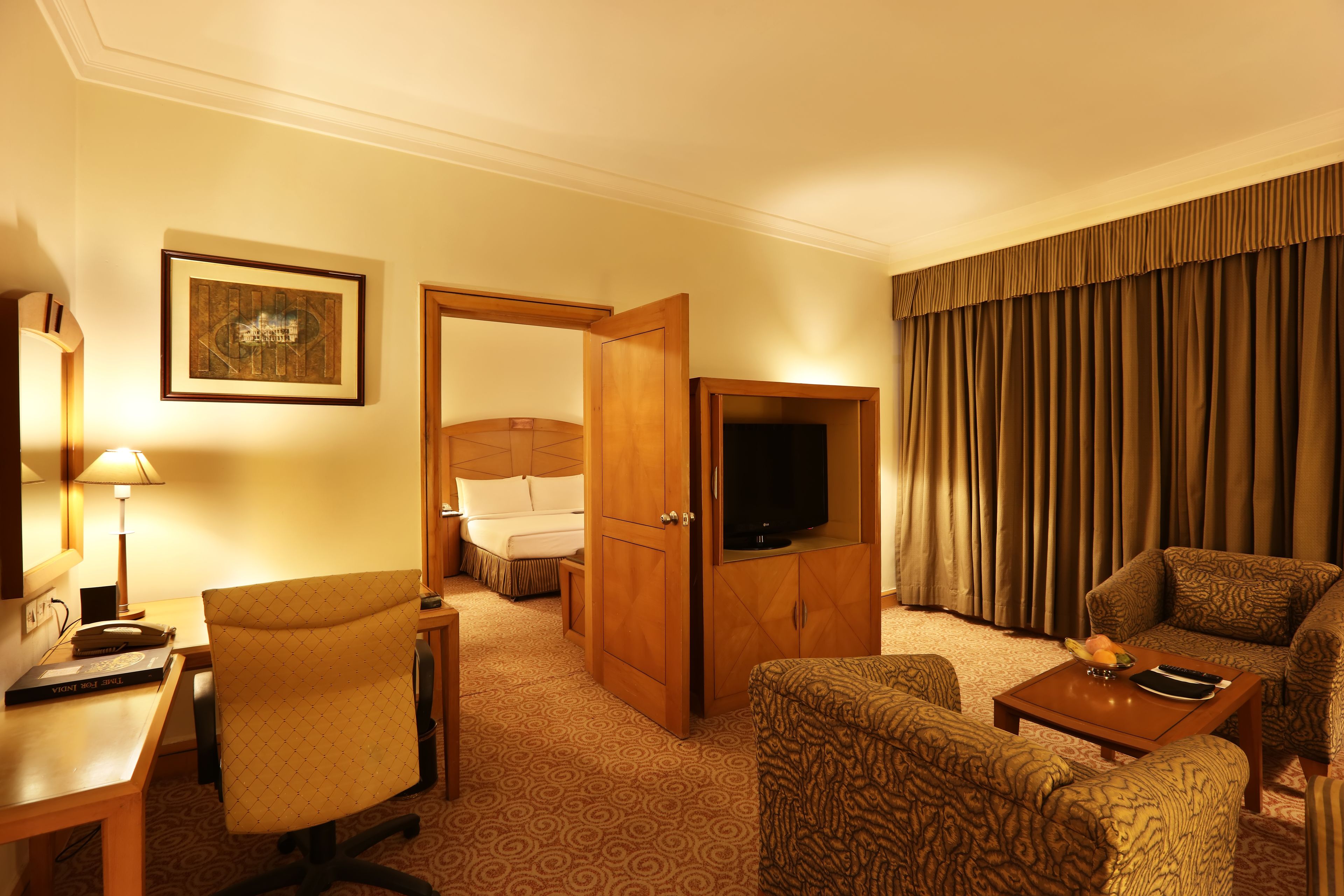 A hotel room with a bed, a TV, a desk with a lamp, and patterned furniture.