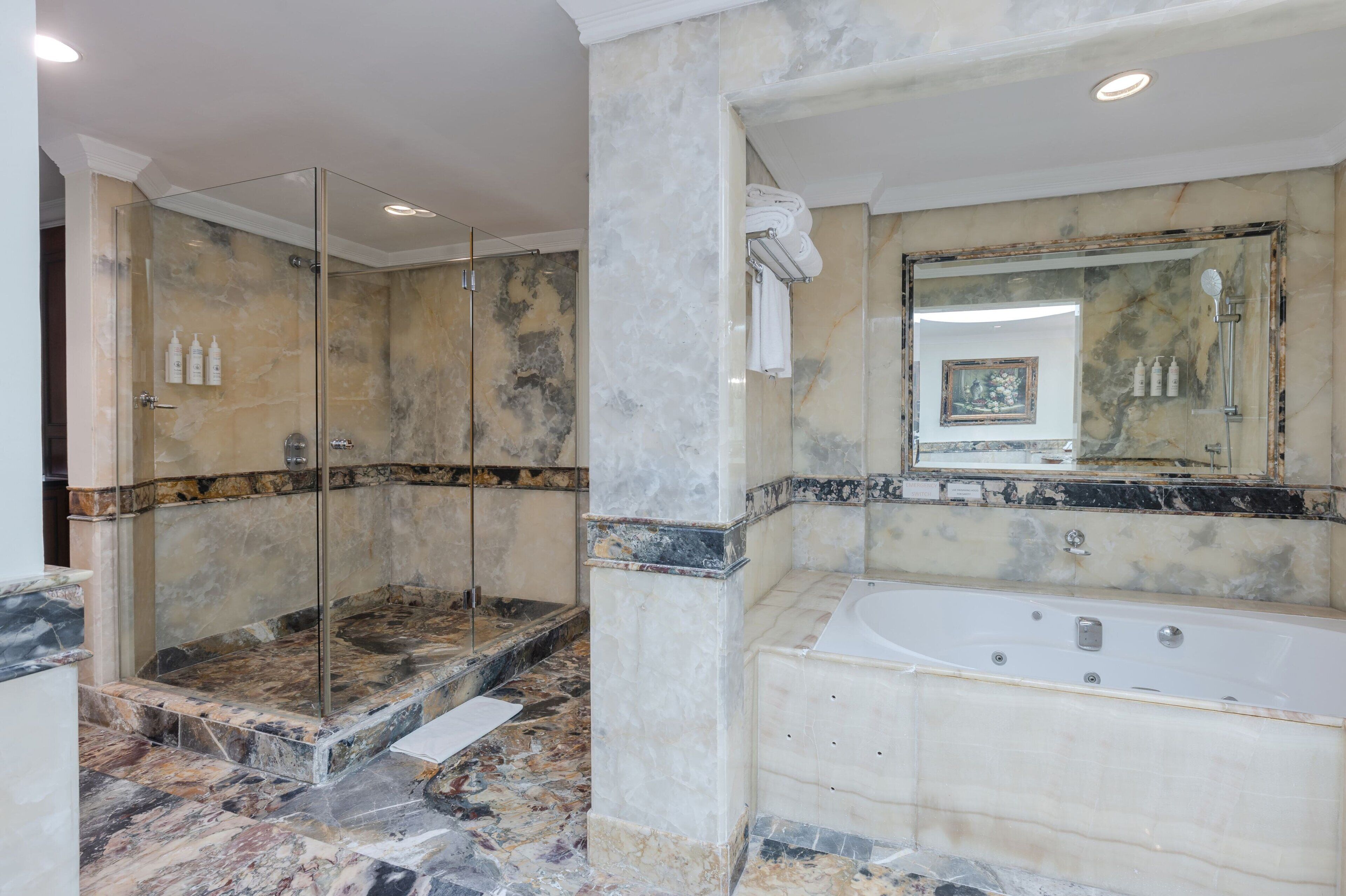 A luxurious bathroom with a glass-enclosed shower, a large bathtub, and marble flooring.
