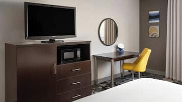 Una habitación de hotel con cama, televisión, microondas, escritorio, silla y cuadros en la pared.