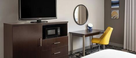 Une chambre d’hôtel équipée d’un lit, d’une télévision, d’un four à micro-ondes, d’un bureau, d’une chaise et d’œuvres d’art accrochées au mur.