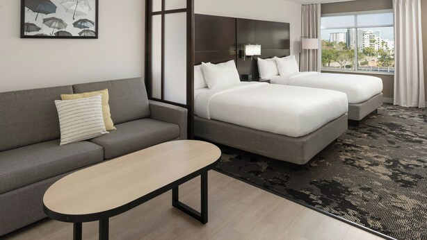 Une chambre d’hôtel avec un canapé, deux lits, une table et une vue sur les immeubles.