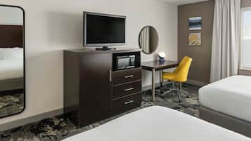 Una habitación de hotel con cama, escritorio, televisión, silla y espejo.