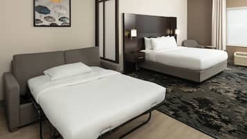 A hotel room with a double bed, a single bed, a sofa, a desk, and a chair.
