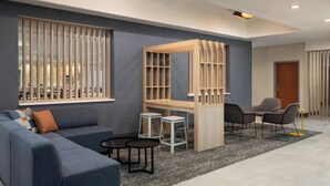 Un espace détente moderne comprenant un canapé bleu, deux petites tables, une cloison en bois avec des étagères et deux fauteuils.