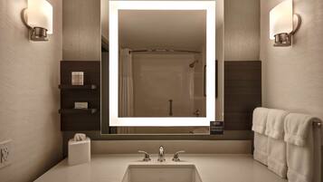 A modern bathroom with a large mirror, two wall-mounted lights, a towel rack, and a shelf with toiletries.