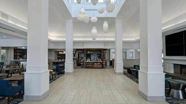 A spacious lobby with a central coffee shop, high ceilings with hanging lamps, and a tiled floor.
