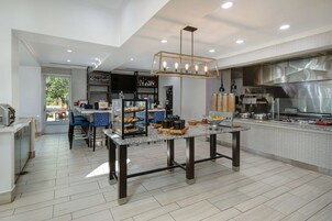 A modern kitchen with a dining area, featuring a granite countertop, a hanging light fixture, and a view of the outdoors.