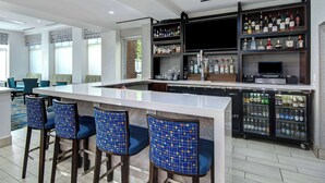 A bar area with a long counter, blue patterned chairs, and shelves stocked with various bottles.