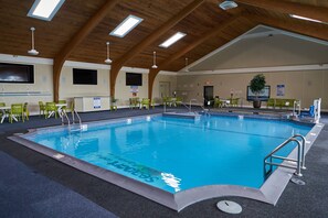 An indoor swimming pool with clear lanes, surrounded by green chairs and tables, under a wooden ceiling with skylights. - Seaport Resort & Marina (Fairhaven)