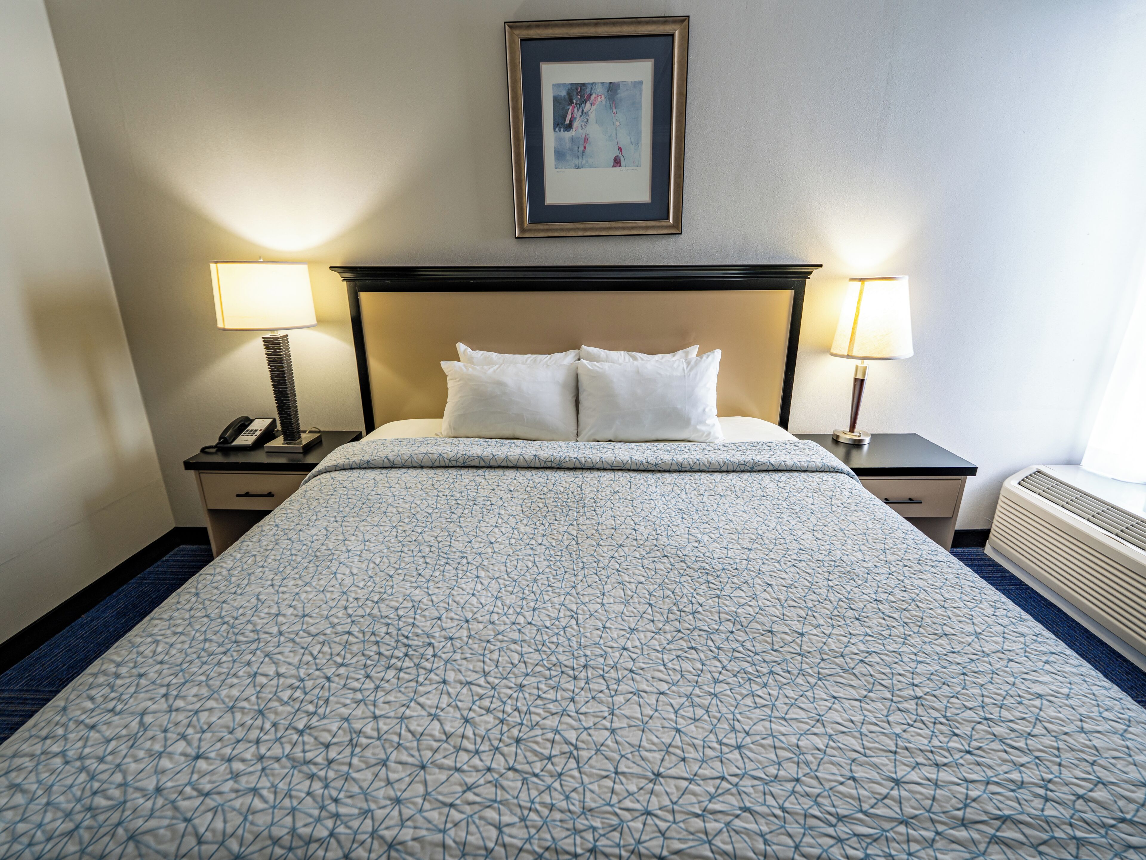 Una habitación de hotel con una cama, dos lámparas de noche, un cuadro en la pared y un calentador.