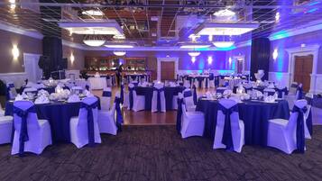 Un salón de banquetes con mesas redondas, sillas blancas y manteles azules.