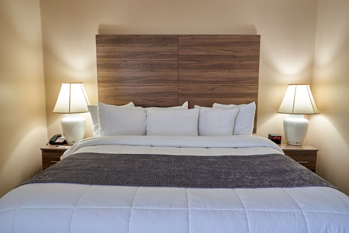 A neatly made bed with white linens, a wooden headboard, and two bedside lamps.