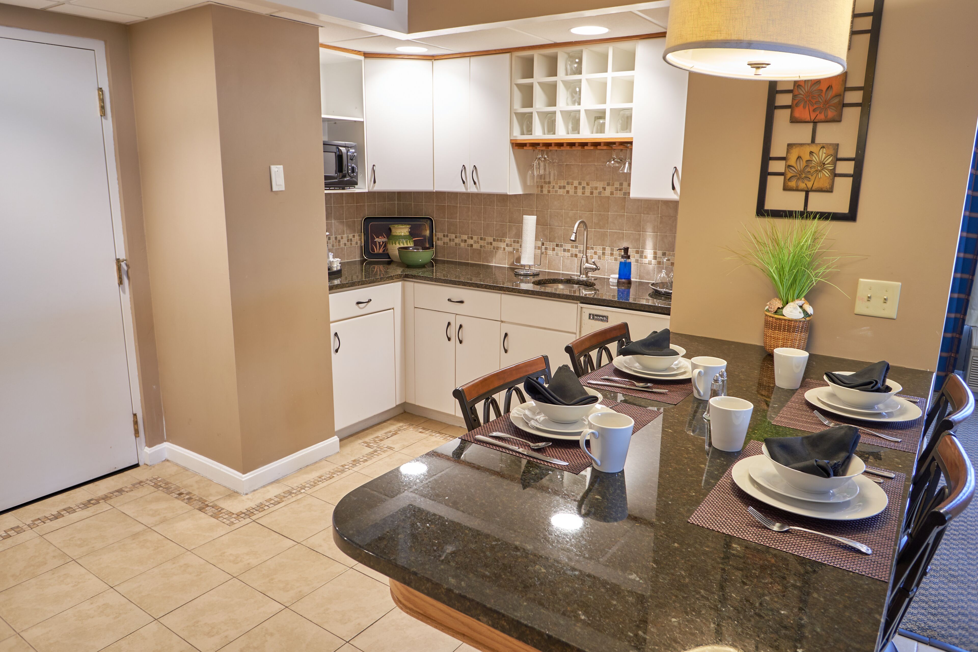 A modern kitchen with white cabinets, a granite countertop, and a dining area set for four.