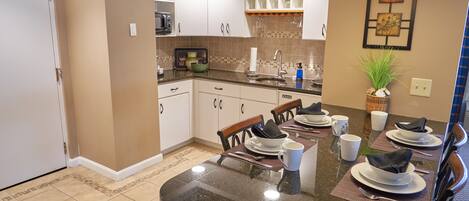 A modern kitchen with white cabinets, a granite countertop, and a dining area set for four.