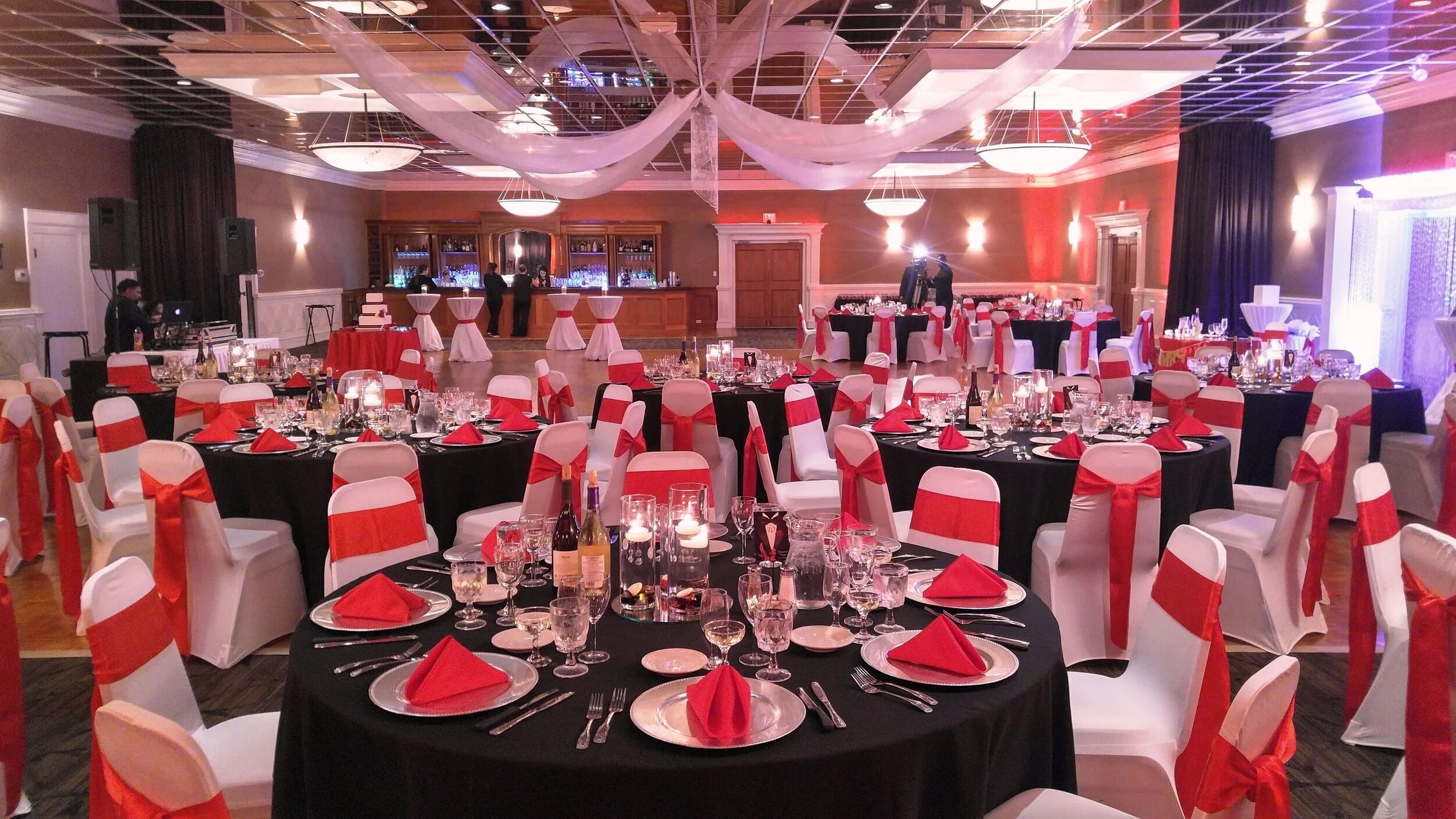 A banquet hall with round tables set for a formal event, featuring white and red decor.